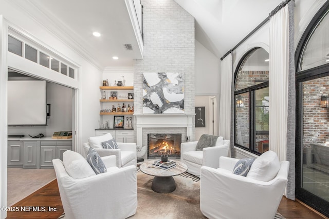 living area with high vaulted ceiling, recessed lighting, a large fireplace, visible vents, and ornamental molding