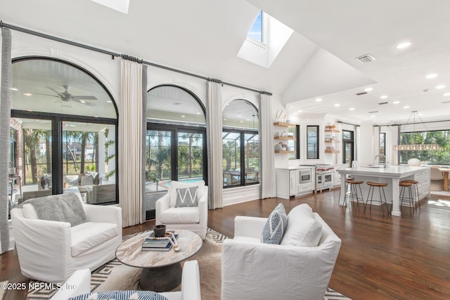 living area with ceiling fan, vaulted ceiling with skylight, recessed lighting, dark wood-type flooring, and visible vents