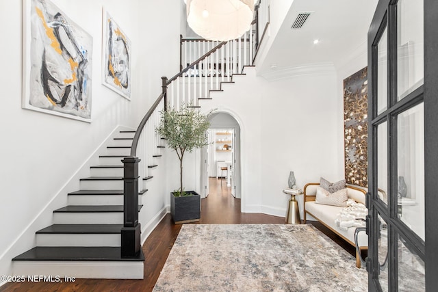 entryway featuring arched walkways, visible vents, a towering ceiling, dark wood-type flooring, and baseboards