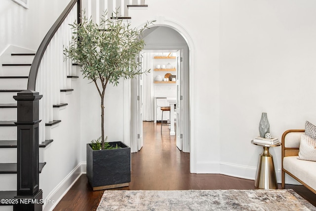 interior space with baseboards, stairs, arched walkways, and dark wood-style flooring