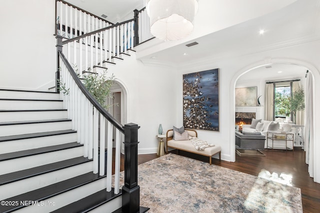 foyer with visible vents, arched walkways, wood finished floors, a lit fireplace, and stairs