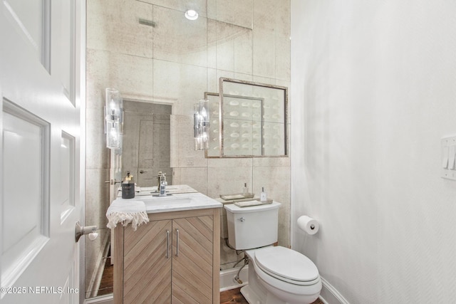 bathroom with toilet, baseboards, tile walls, and vanity