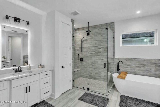 bathroom featuring visible vents, tile walls, a stall shower, a soaking tub, and vanity