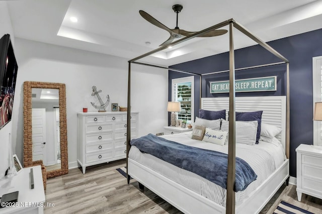 bedroom featuring a raised ceiling, a ceiling fan, wood finished floors, recessed lighting, and baseboards
