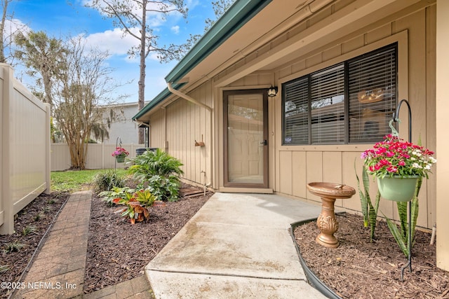 view of exterior entry with board and batten siding and fence