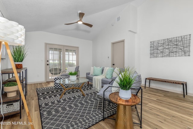 living area featuring lofted ceiling, light wood-style flooring, visible vents, and ceiling fan