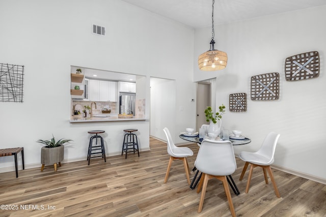 dining room with light wood-style flooring, a high ceiling, visible vents, and baseboards