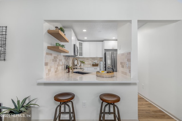 kitchen with open shelves, appliances with stainless steel finishes, white cabinetry, a sink, and a kitchen bar