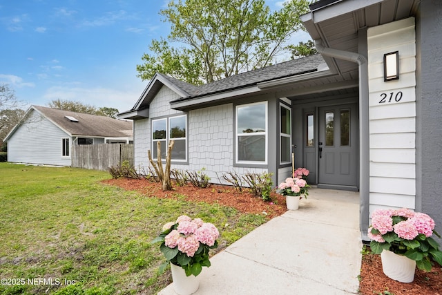 entrance to property featuring a shingled roof, fence, and a yard