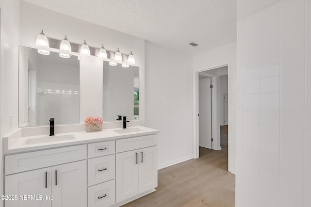 full bathroom with visible vents, a sink, a textured ceiling, and wood finished floors