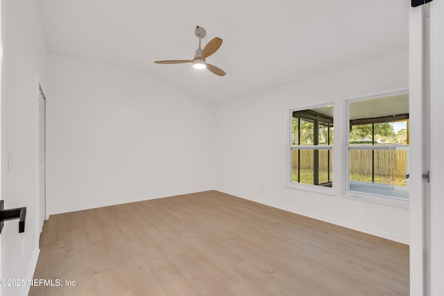 spare room with light wood-style floors, baseboards, vaulted ceiling, and a ceiling fan