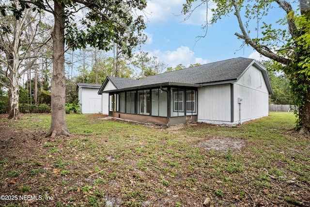 rear view of house with a yard, roof with shingles, and a sunroom