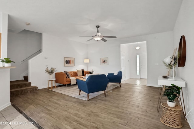 living area with light wood-style floors, a ceiling fan, baseboards, and stairs