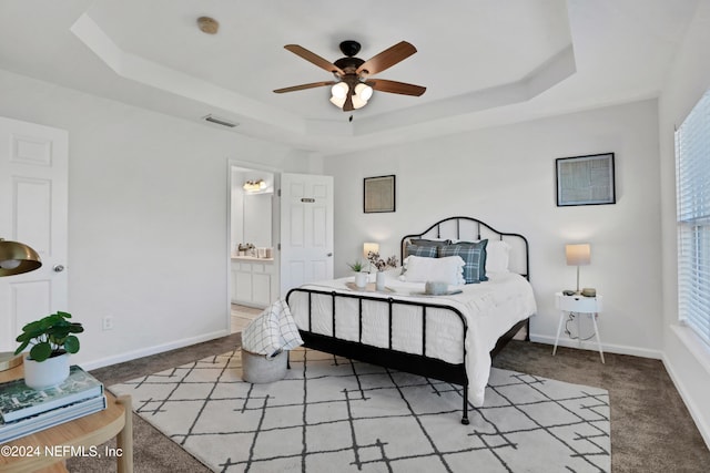 carpeted bedroom with a raised ceiling, visible vents, a ceiling fan, connected bathroom, and baseboards