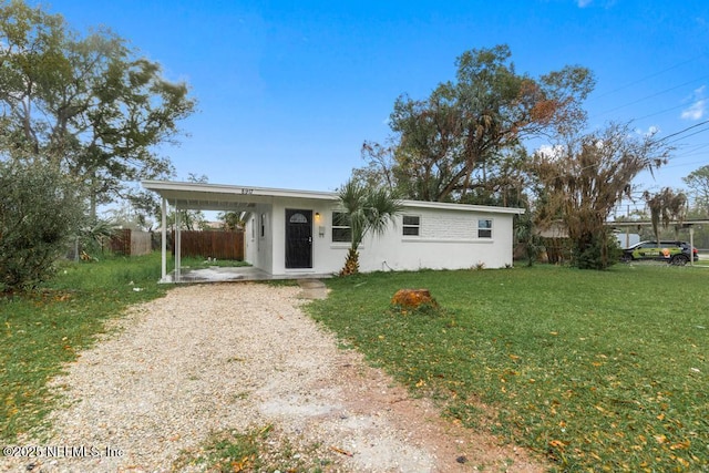 ranch-style home featuring gravel driveway, fence, a front lawn, and an attached carport