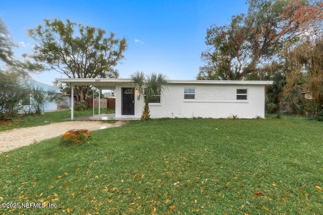 ranch-style house with gravel driveway, stucco siding, fence, a carport, and a front lawn