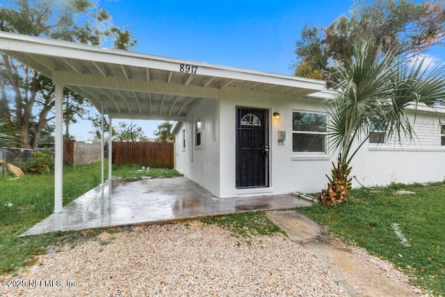 doorway to property with fence, a lawn, and stucco siding