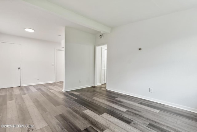 empty room with beam ceiling, visible vents, baseboards, and wood finished floors