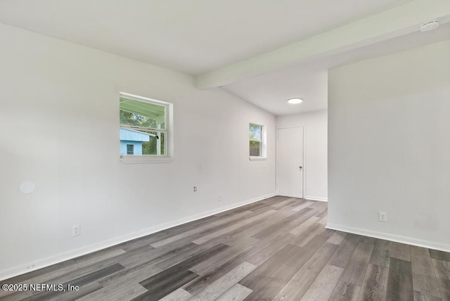 unfurnished room featuring baseboards, beamed ceiling, wood finished floors, and a healthy amount of sunlight