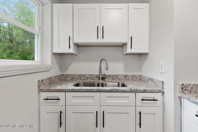 kitchen with light stone countertops, white cabinets, a sink, and a textured wall