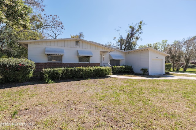 single story home featuring a garage, brick siding, driveway, board and batten siding, and a front yard