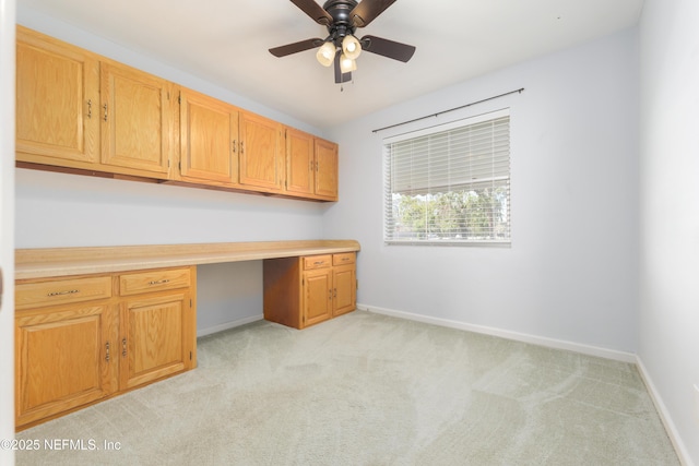 unfurnished office featuring built in desk, a ceiling fan, light colored carpet, and baseboards