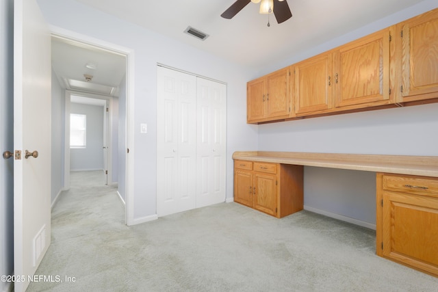 unfurnished office with baseboards, built in desk, visible vents, and light colored carpet