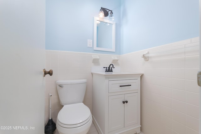 bathroom featuring a wainscoted wall, vanity, toilet, and tile walls