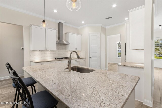 kitchen featuring a sink, visible vents, white cabinetry, wall chimney exhaust hood, and tasteful backsplash