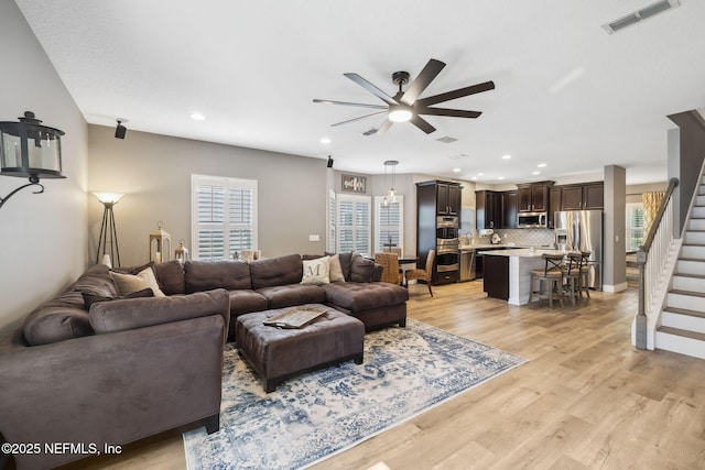 living area with light wood finished floors, stairs, visible vents, and a ceiling fan