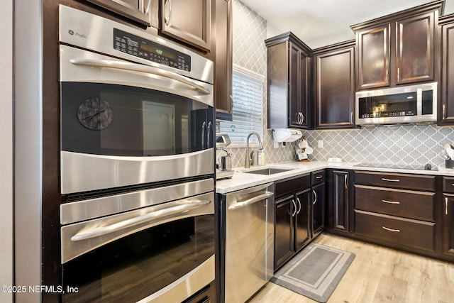 kitchen with backsplash, appliances with stainless steel finishes, a sink, dark brown cabinets, and light wood-type flooring