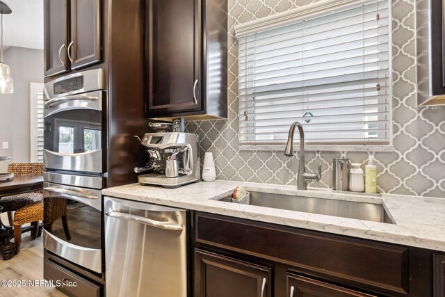 kitchen featuring dark brown cabinetry, decorative backsplash, appliances with stainless steel finishes, light stone counters, and a sink