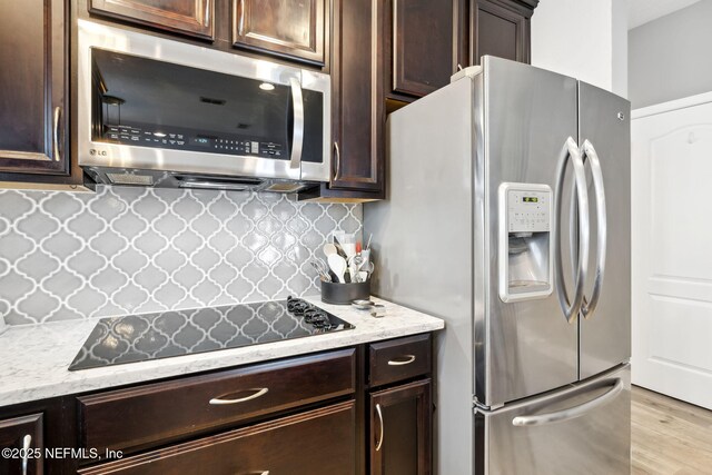 kitchen featuring tasteful backsplash, light wood-style flooring, light stone countertops, stainless steel appliances, and dark brown cabinets