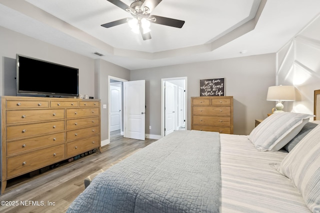 bedroom with a ceiling fan, visible vents, baseboards, light wood-type flooring, and a tray ceiling