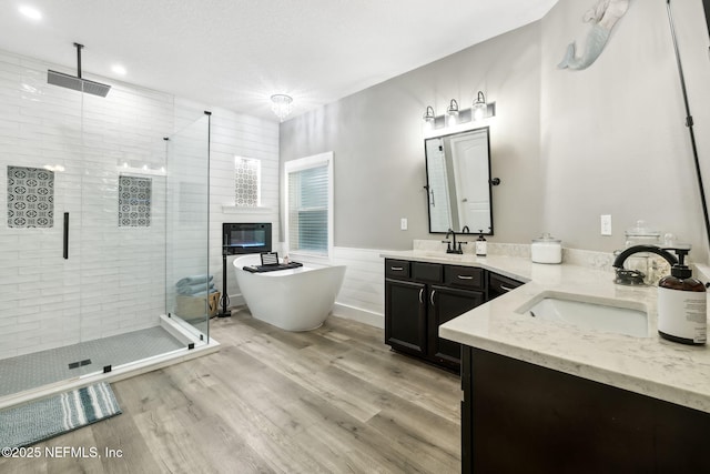 bathroom featuring a textured ceiling, wood finished floors, vanity, a freestanding bath, and a stall shower