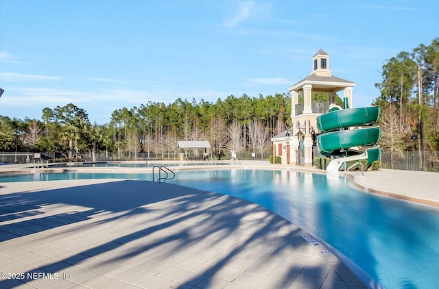 community pool with fence, a water slide, and a patio