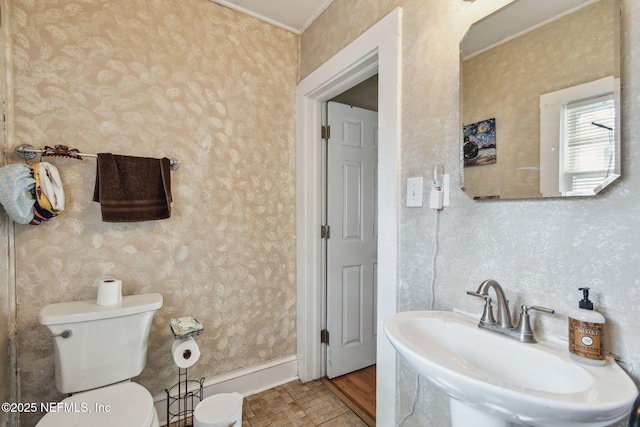 bathroom with a sink, toilet, and wallpapered walls