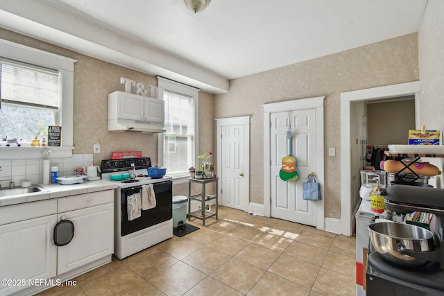 kitchen with light tile patterned floors, range with electric cooktop, a sink, white cabinets, and tile counters