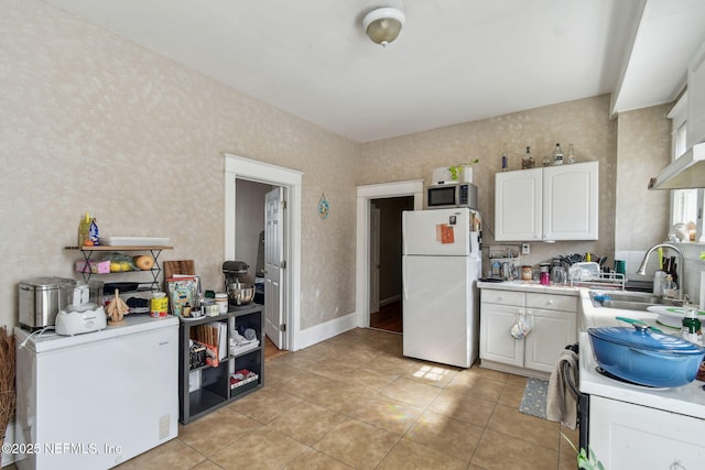 kitchen featuring light tile patterned floors, white appliances, a sink, white cabinets, and light countertops