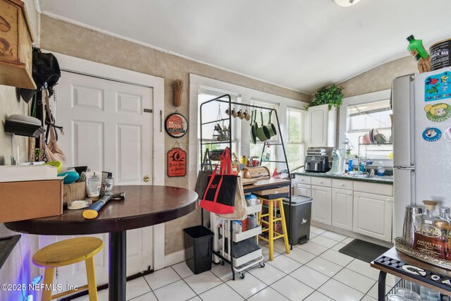 kitchen with lofted ceiling, light tile patterned flooring, white cabinets, and freestanding refrigerator