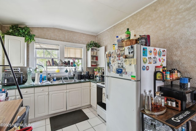 kitchen with dark countertops, white cabinets, a sink, light tile patterned flooring, and white appliances