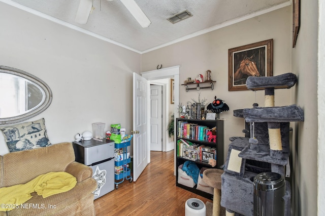 interior space with visible vents, ornamental molding, ceiling fan, a textured ceiling, and wood finished floors