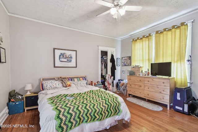 bedroom with ceiling fan, wood finished floors, crown molding, a textured ceiling, and a closet