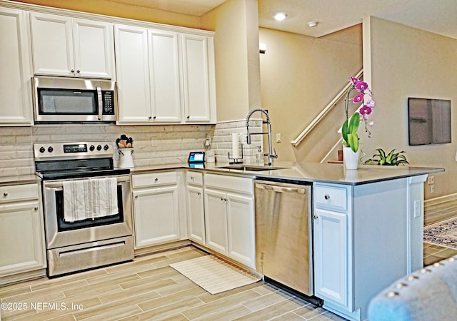 kitchen featuring appliances with stainless steel finishes, a sink, a peninsula, and decorative backsplash