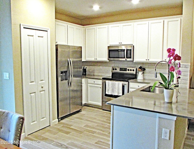 kitchen featuring appliances with stainless steel finishes, white cabinetry, a peninsula, and tasteful backsplash