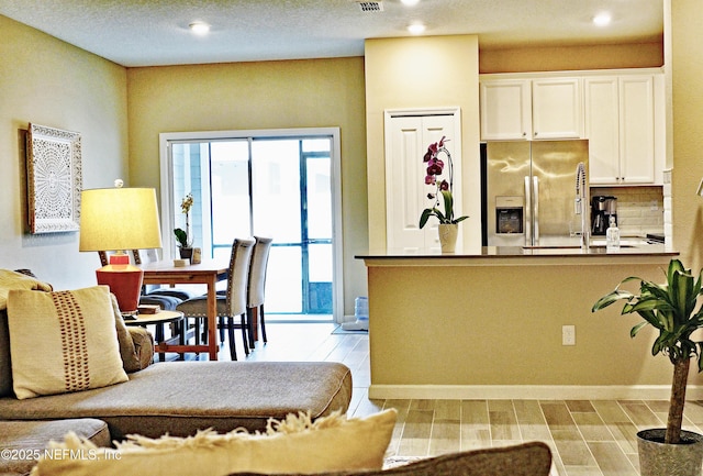 kitchen with wood tiled floor, white cabinetry, stainless steel refrigerator with ice dispenser, and a peninsula