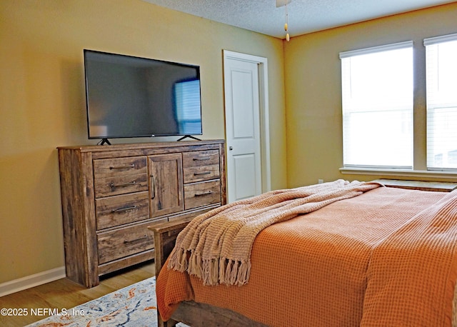 bedroom with a textured ceiling, baseboards, and wood finished floors