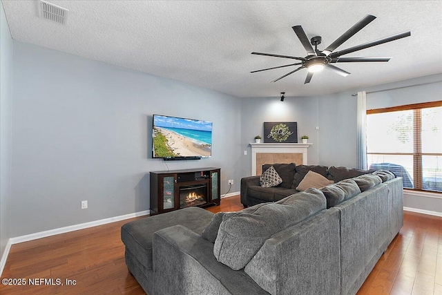 living area featuring visible vents, baseboards, ceiling fan, a tiled fireplace, and hardwood / wood-style flooring