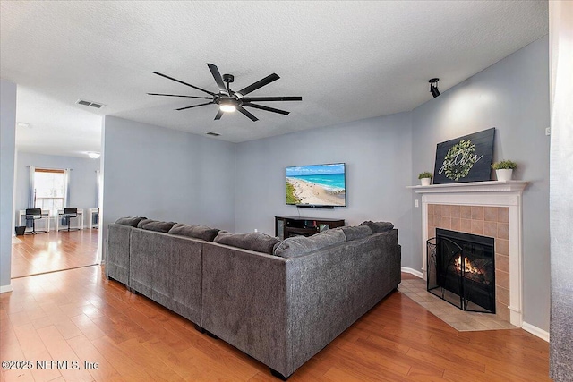 living room with visible vents, ceiling fan, a tiled fireplace, wood finished floors, and a textured ceiling