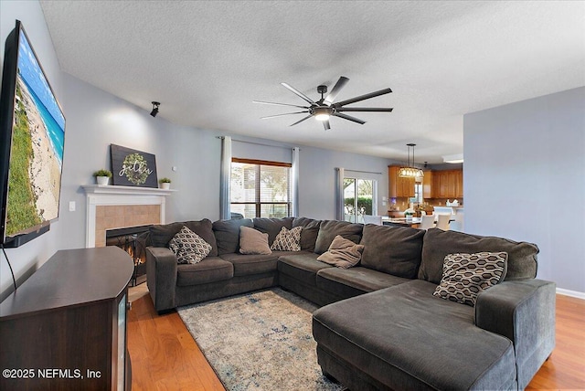 living room featuring a fireplace, a textured ceiling, light wood-style floors, and a ceiling fan